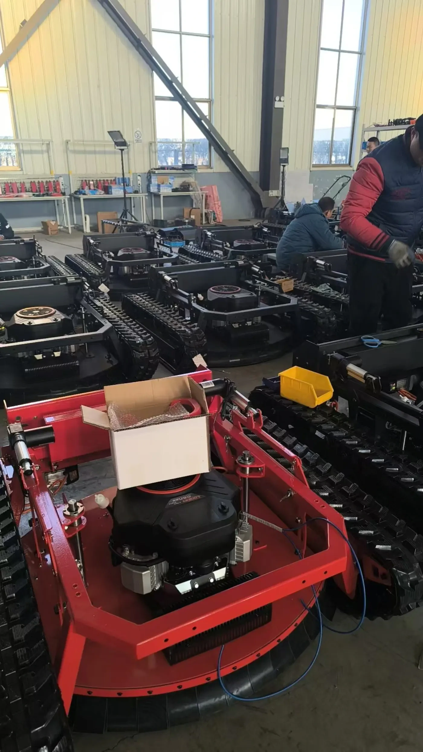 Assembly work taking place around rows of tracked mower chassis